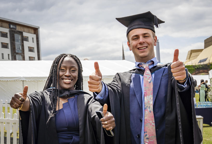 A man and woman who have graduated have their thumbs up