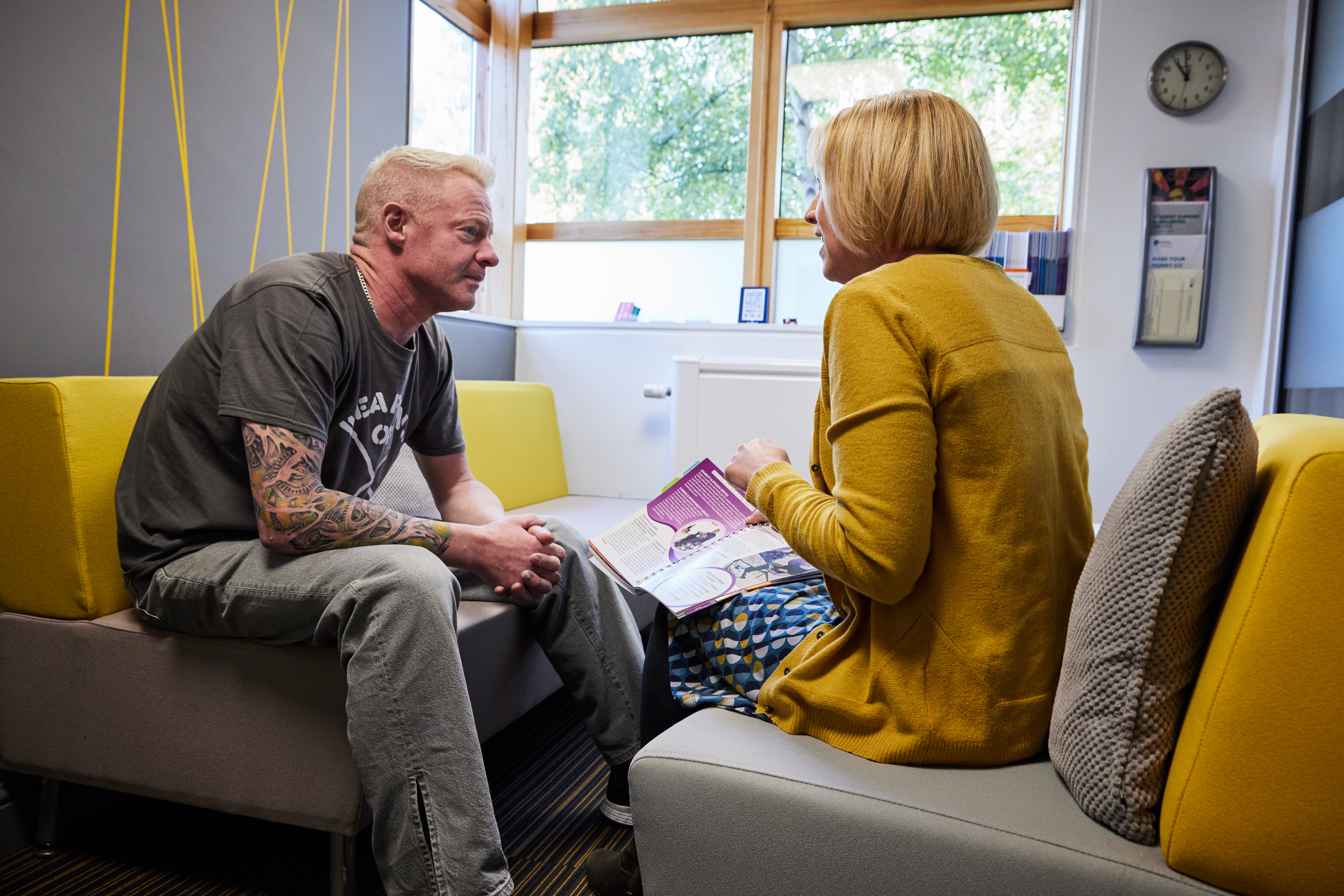 A man sits on a cushioned chair listening to advice from a lady sat opposite