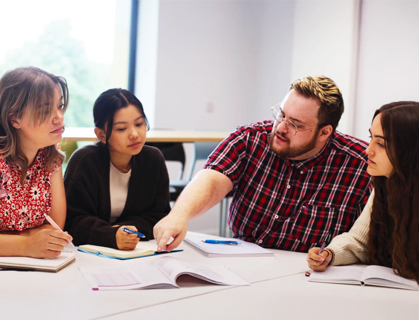 Students sat around a table discussing information in a textbook