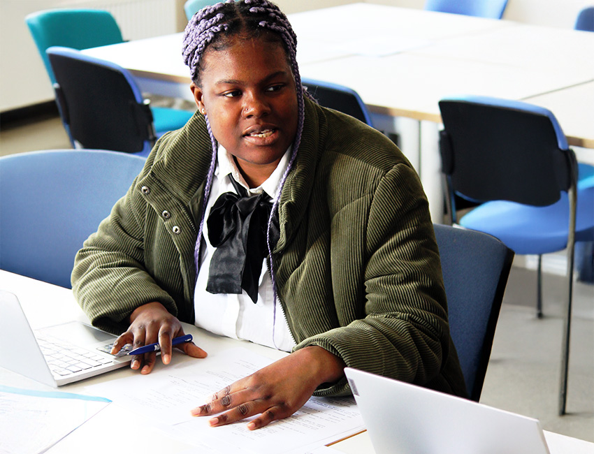 Student at a desk with laptops and printed out pages of a screenplay on the table