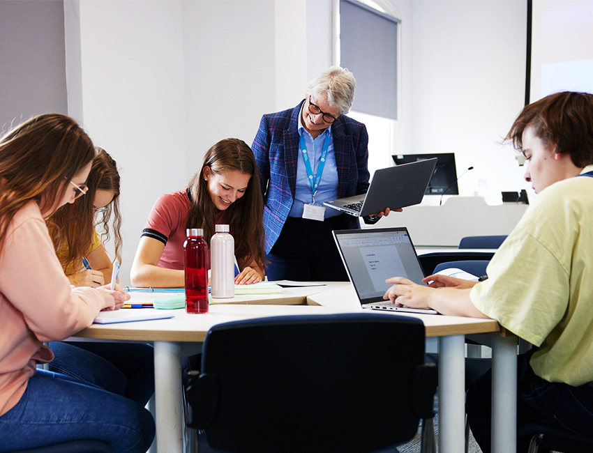 Students working in a classroom with their teaching offering support