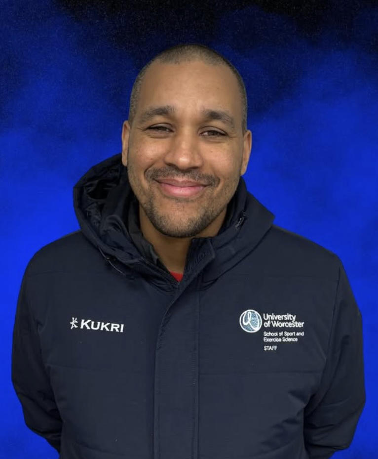 Alexis Lewis poses in a dark blue coat against a lighter blue background