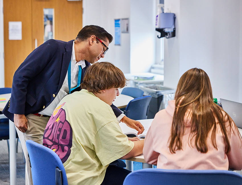 A lecturer stood talking to two students sat in the classroom