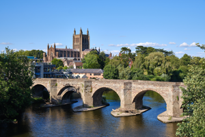 View of Hereford Cathedral in the distance beside the River Wye with a bridge crossing the river.