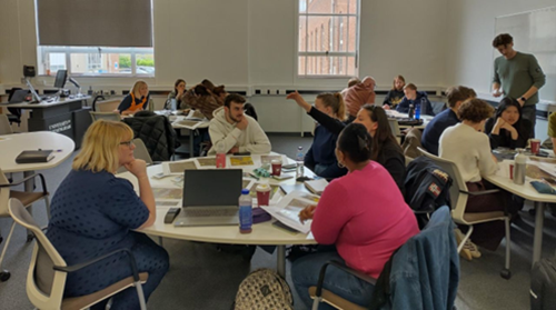 Colleagues grouped together at four tables in a meeting room as part of the Inclusion by Design Research Group Community