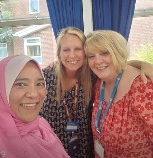Three attendees at the conference grouped together smiling at the camera standing in front of a window.