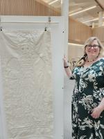 Lucie Bea Dutton poses next to a stitchwork on display in the Hive