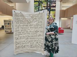 Lucie Bea Dutton poses next to a stitchwork of a list written by Cromwell
