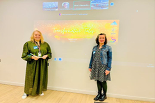 Organisers of the Transformative Tales Event standing either side of the event banner being displayed on a light coloured wall.