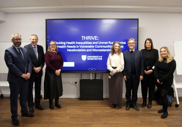 Members of the THRIVE team and their associates pose for a photo by a large screen with details of the THRIVE programme on it