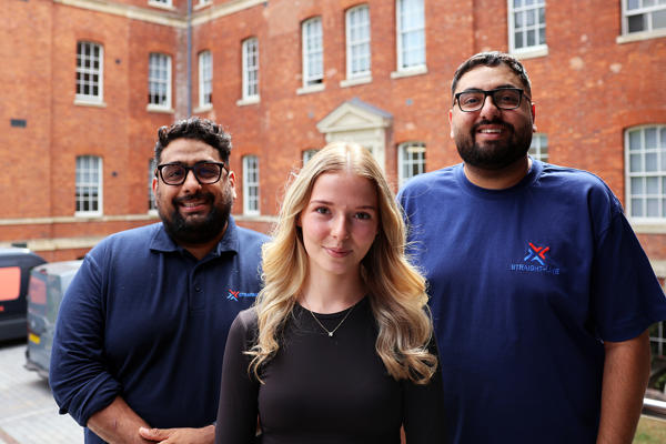 Student Beth Lammas poses with her employers in front of a red brick building