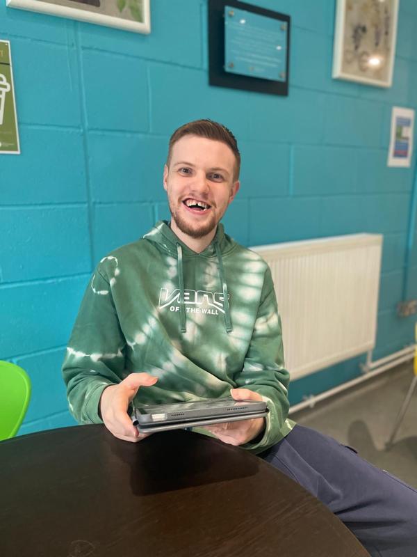 Christian sits with his ipad in a green hoody and smiles at the camera
