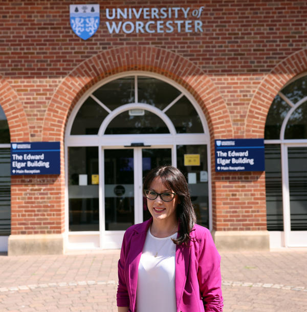 Dr Samantha Pickles outside the University's main entrance in a pink blazer