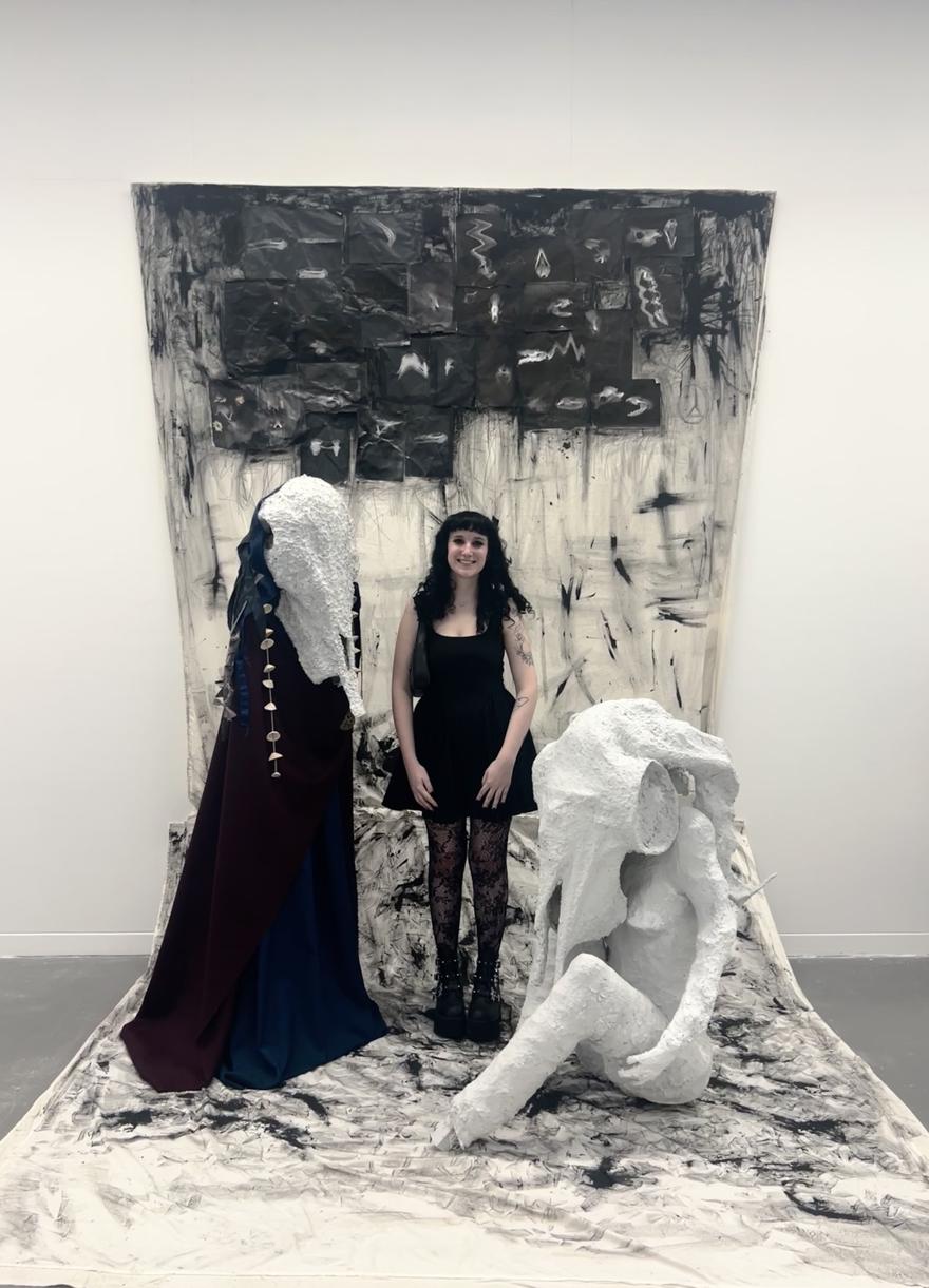 A student poses among a black and white sculptural artwork in a white room