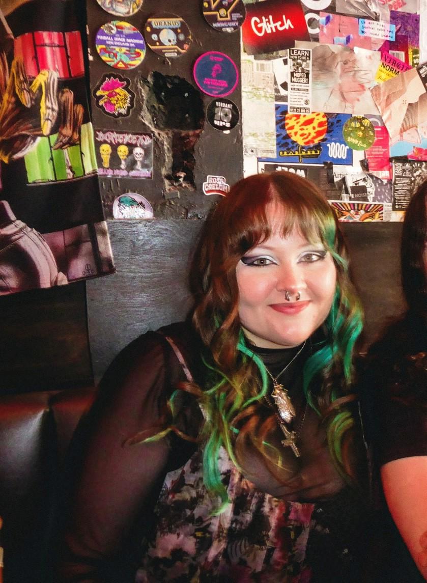 A student poses against a black wall with colourful artwork