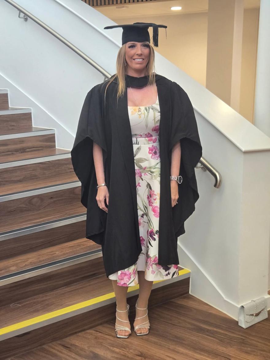 A student poses in graduation gown by some stairs