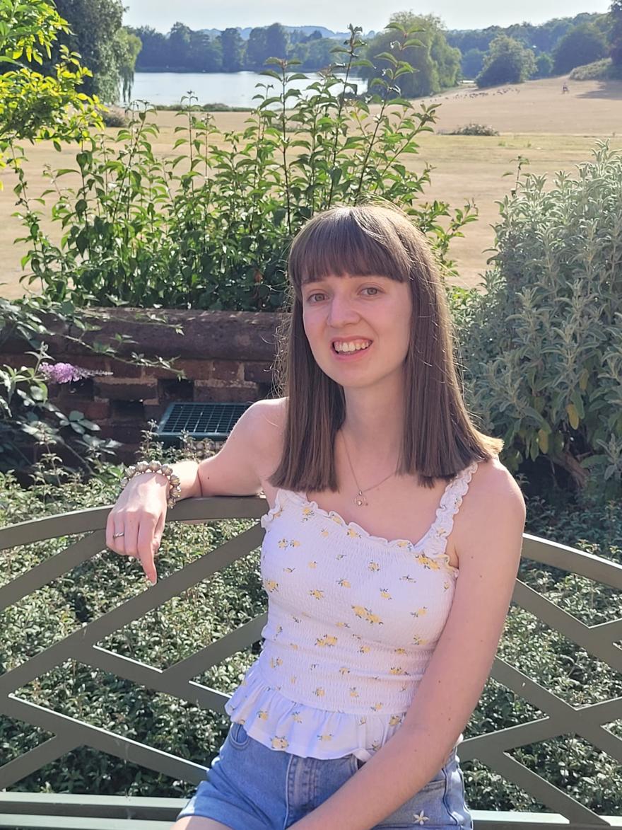 A student poses on a bench with a meadow and lake in the background