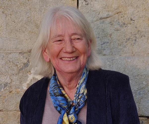 Author Joanna Mack smiles at the camera wearing a dark coloured blazer and blue scarf