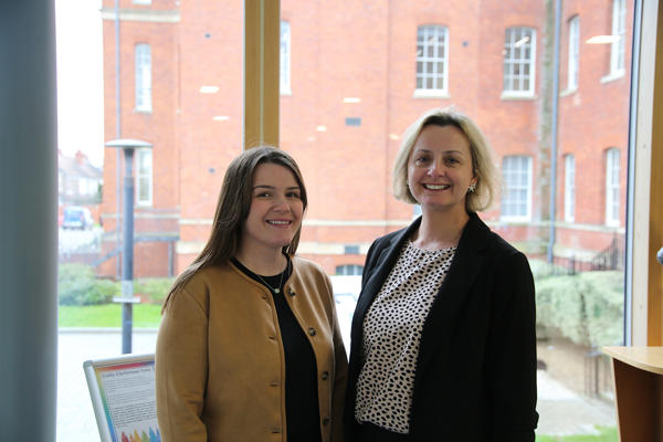Laura Swain and Helen Watts pose in front of a large window