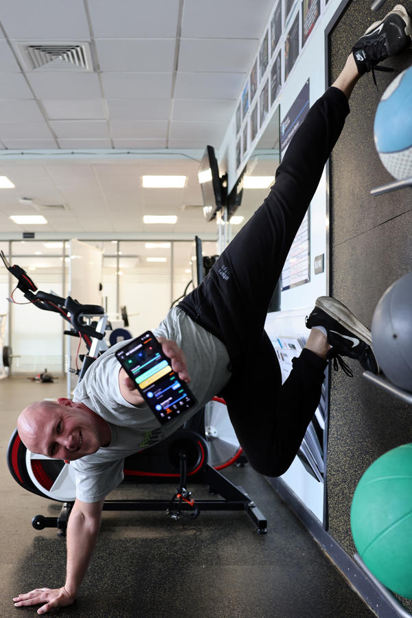 Matt Davies poses in a one handed hand stand while holding his phone out
