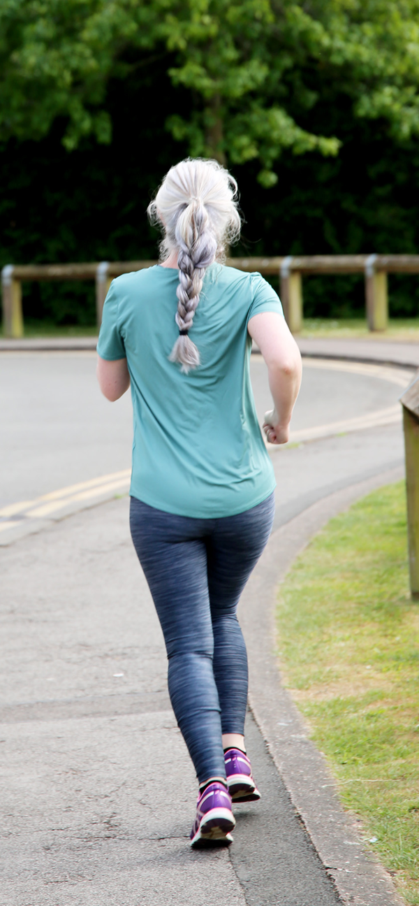 A woman with long platinum blonde hair runs along a path wearing a teal running top.