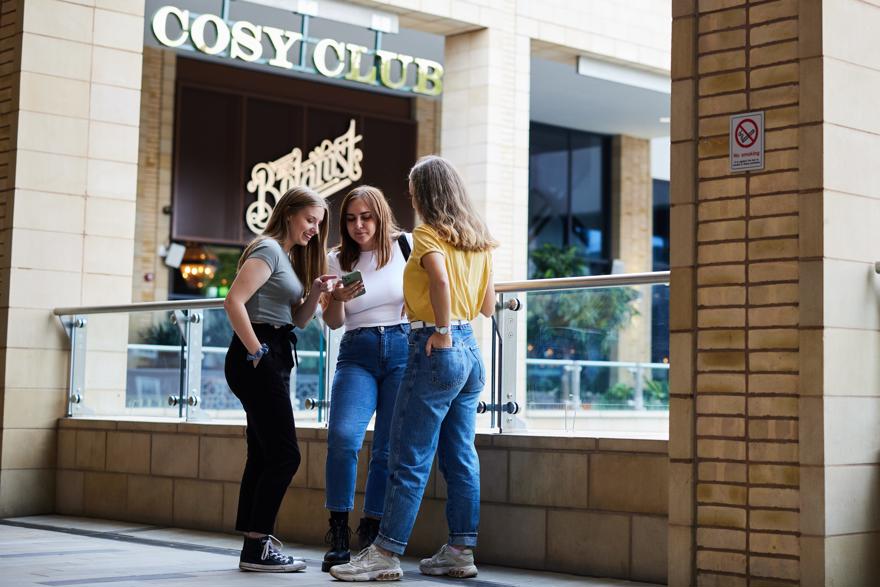 Students gathered around a mobile phone with a restaurant in the background