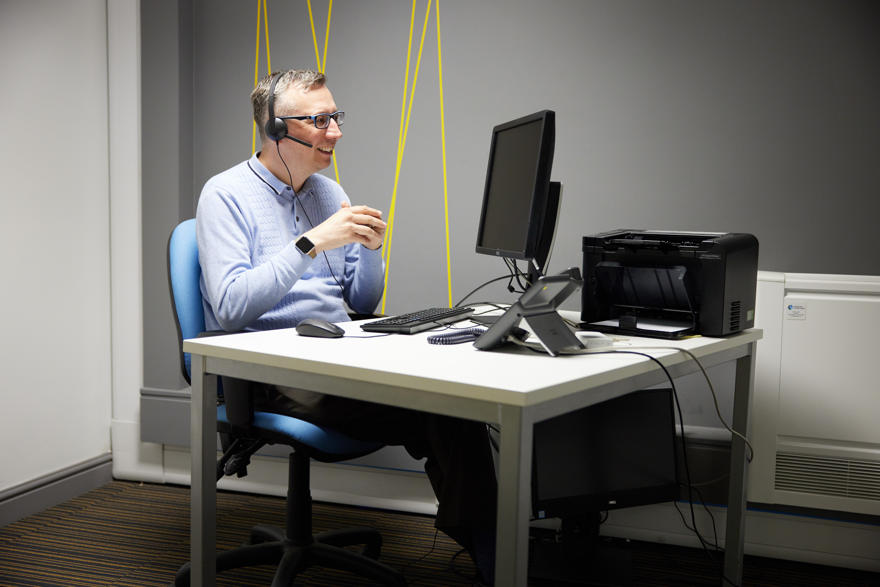 A man, a disability and dyslexia advisor, sits at a desk wearing a headset whilst on a video call