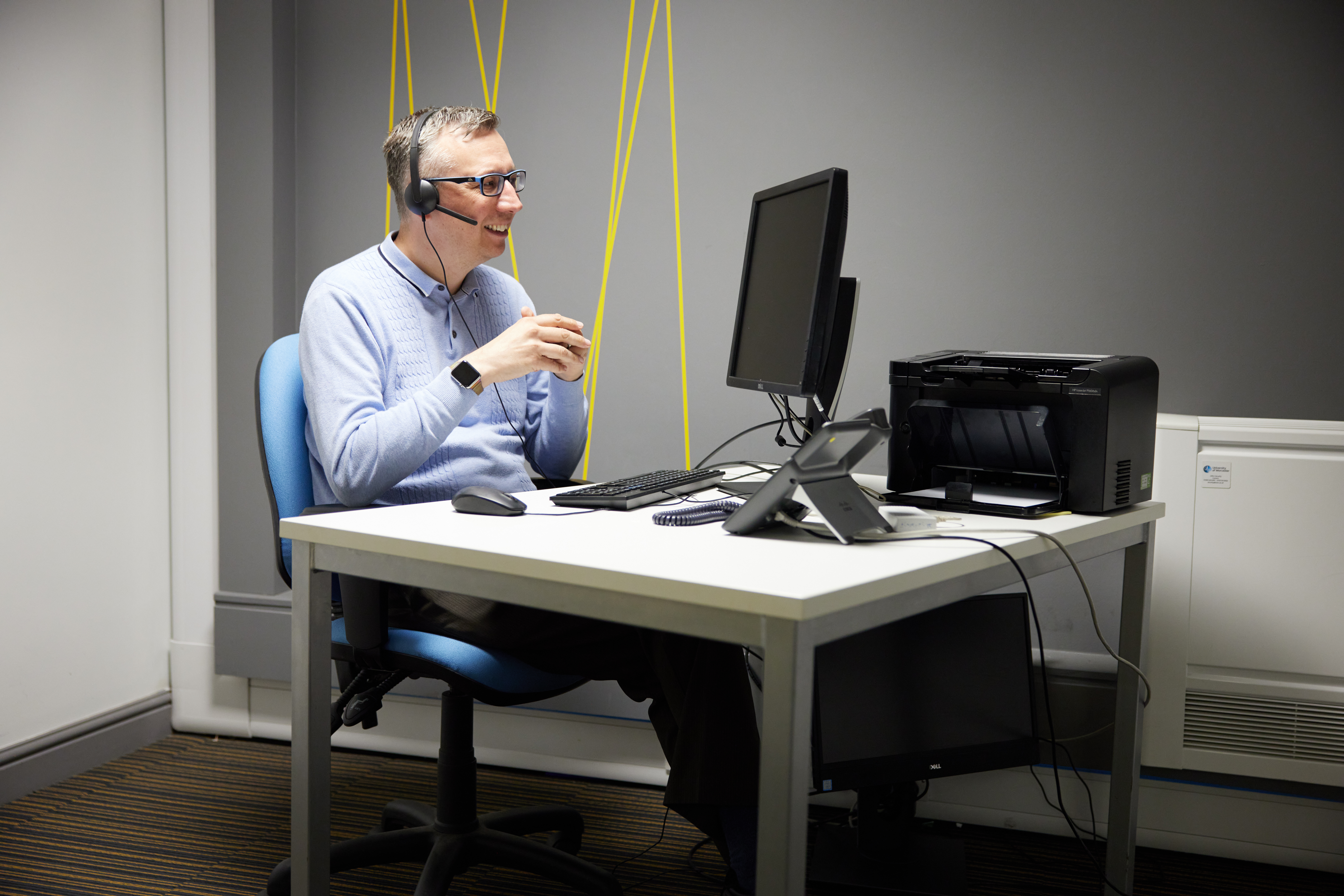 A man sits at a desk wearing a headset whilst on a video call