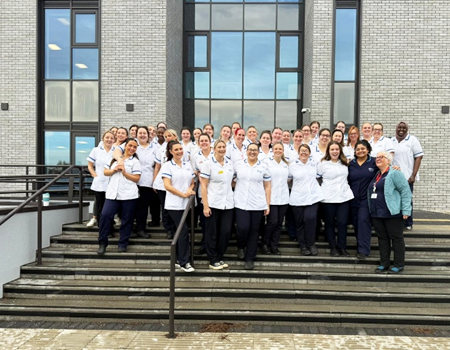 A group photo of midwifery students stood on the steps outside a university building
