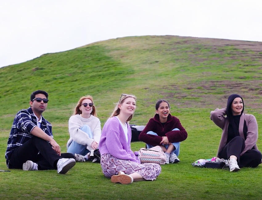 A group of students sat on grass with the peak of a hill behind them