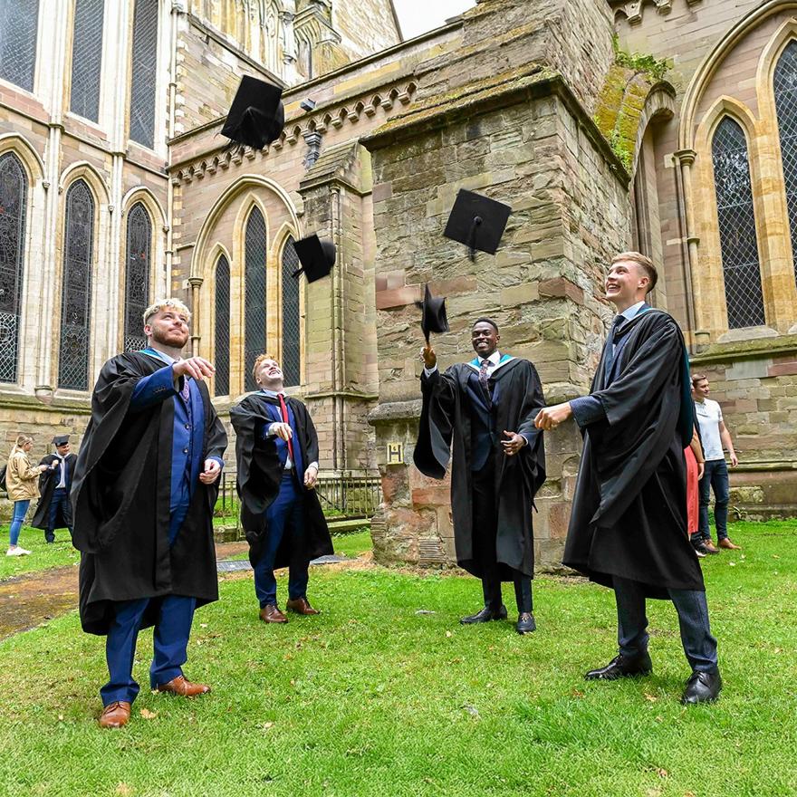 Four male students throwing graduation caps