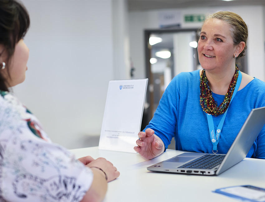 Memeber of student services sat at a table with a student offering information and advice