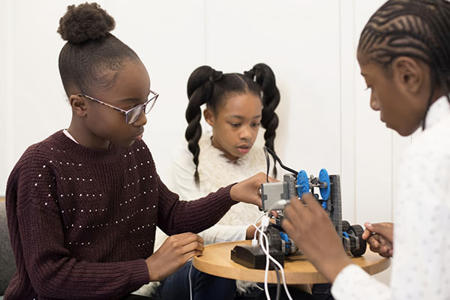 Two children are having a piece of tech demonstrated to them