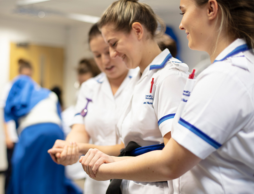 Three nursing students, with two supporting the middle by her forearms