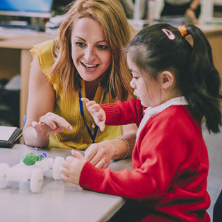 A female teacher is helping a child build a car from plastic