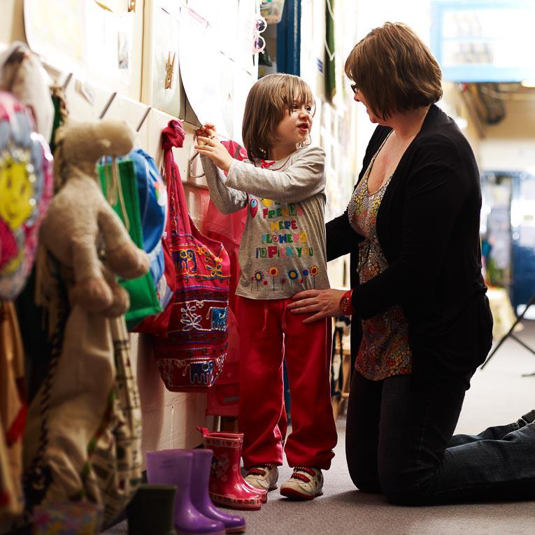 Mother helping child hang coat up at nursery