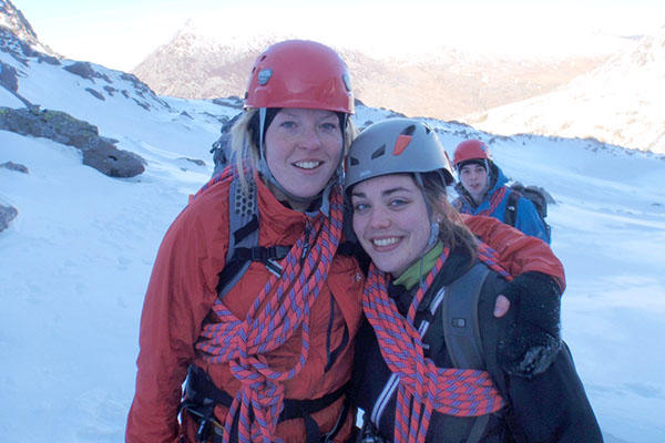 Two women with climbing gear standing on a snowy mountain