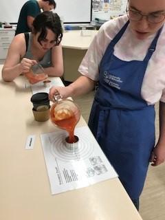 student in blue pouring liquid into a jug