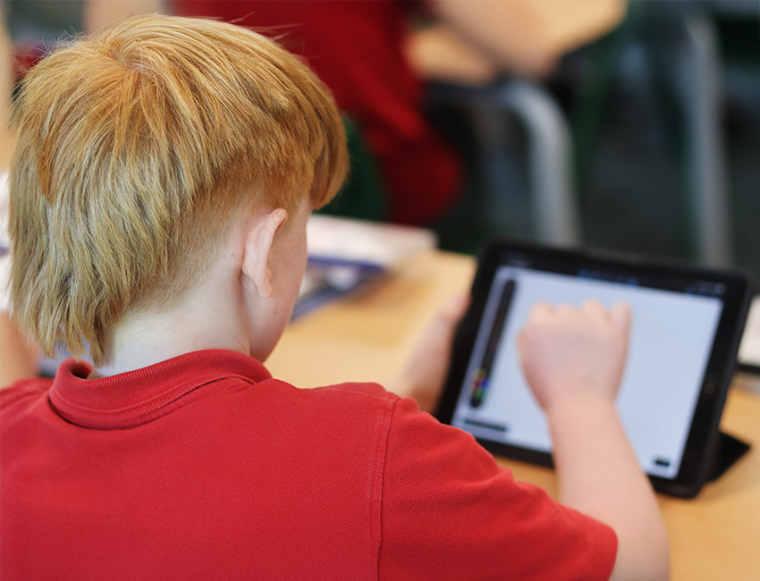 A primary school aged child in school uniform, using a tablet in a classroom