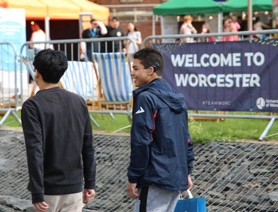 Two students walking with a banner reading "Welcome to Worcester" behind them