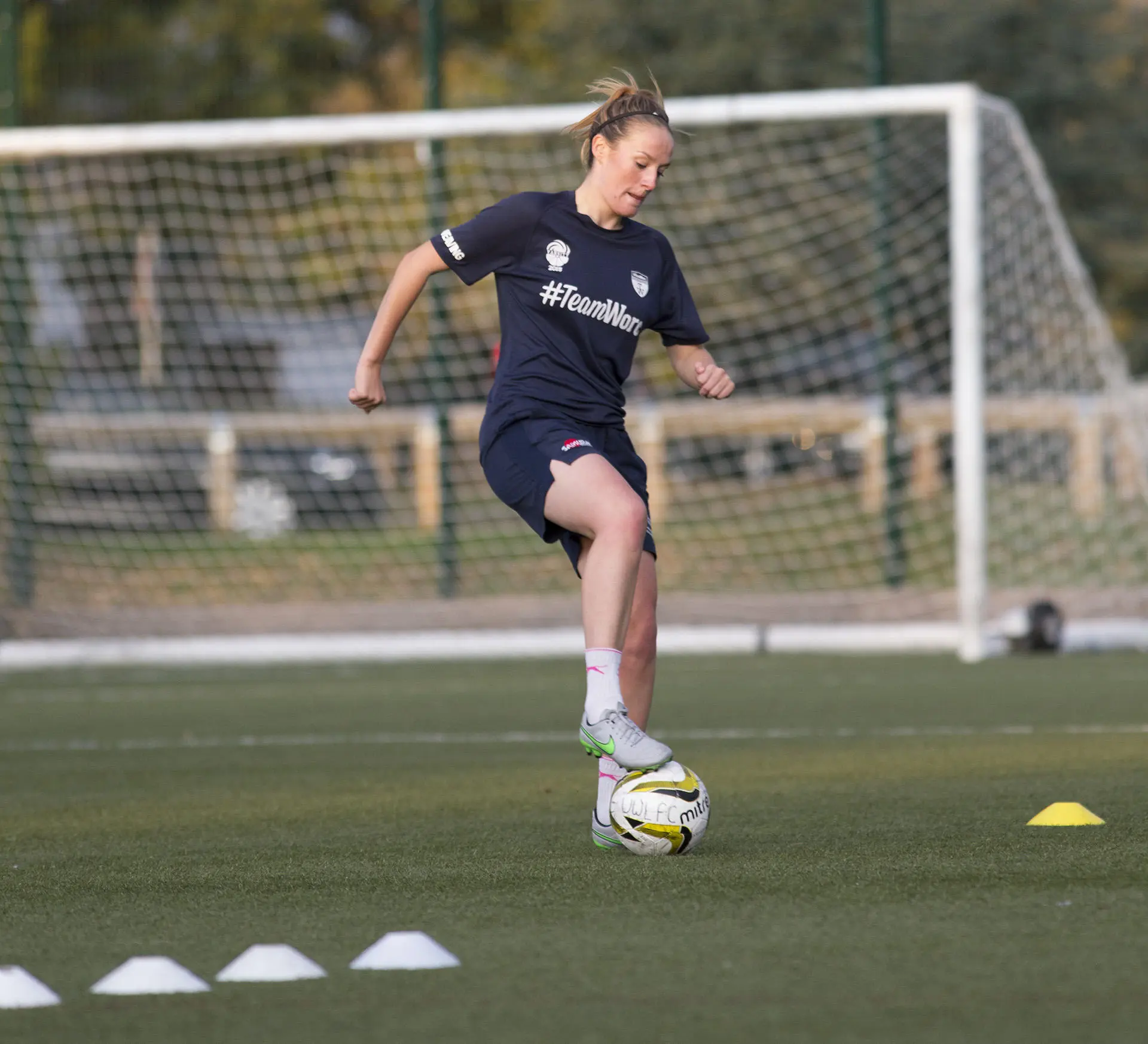A student running a football drill on an astroturf pitch