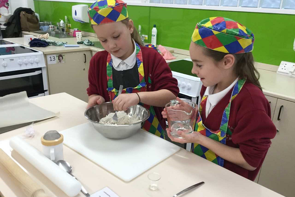 two school pupils with chequered hats with a mixing bowl