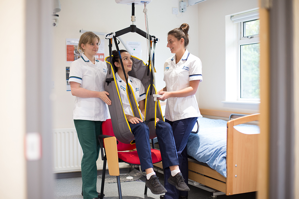two students standing either side of a third student who is sitting in a sling