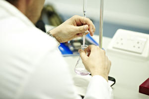laboratory technician in a white protective jacket holding conical flask and probe