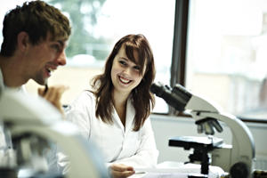 two students in white protective clothing beside a microscope