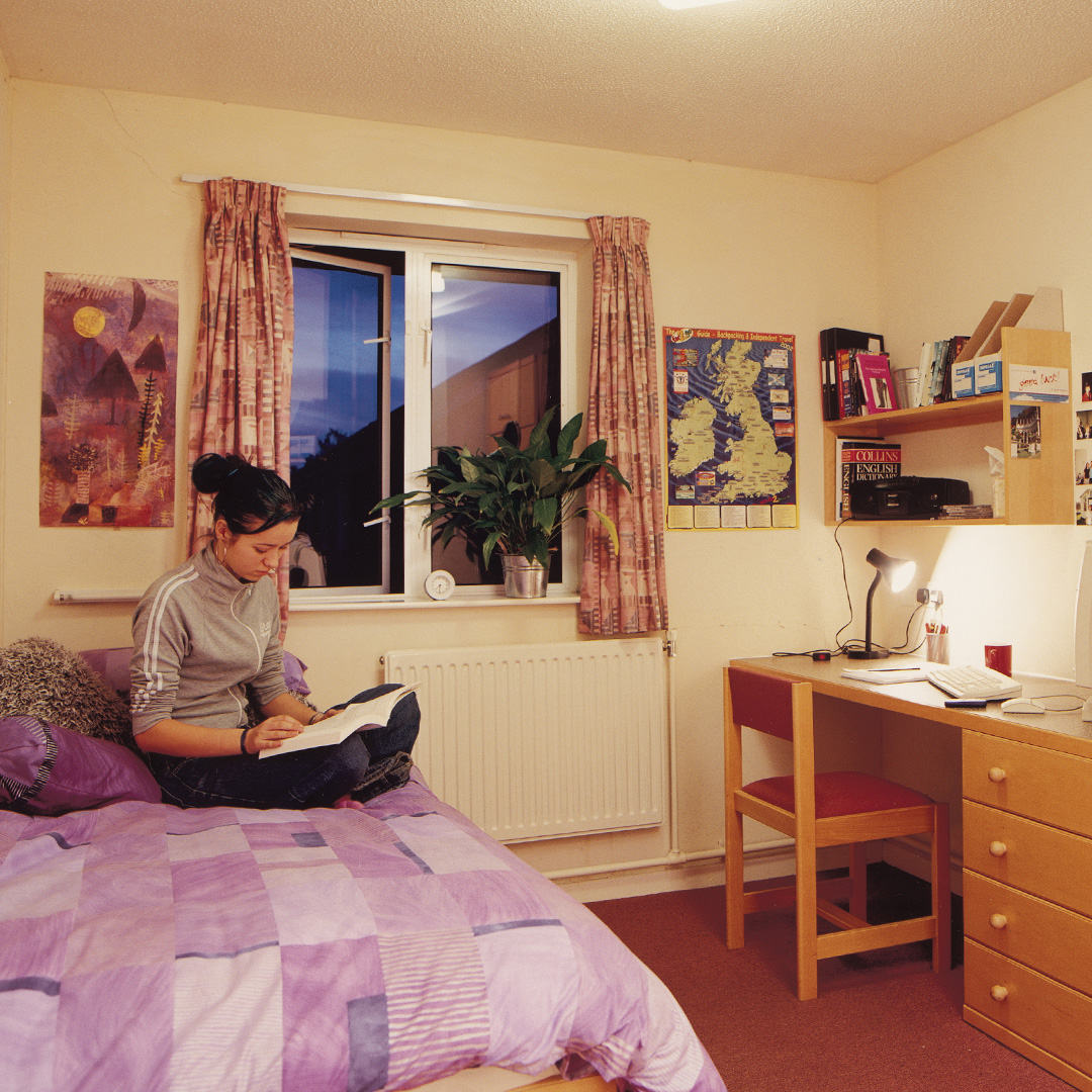 A student writing in a notebook in their bedroom in student halls
