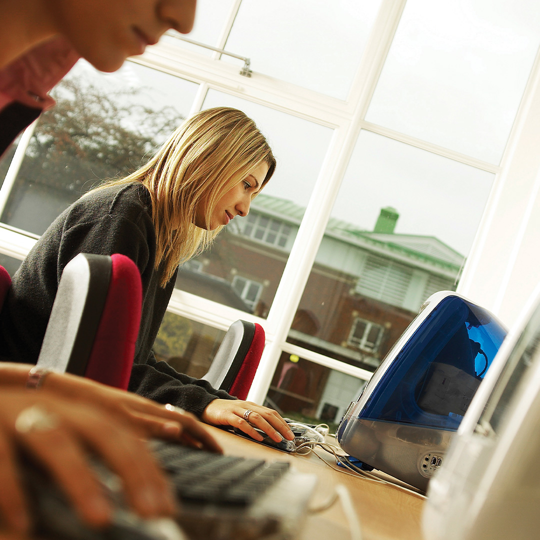 Young woman focused on typing at a desktop computer in a bright room