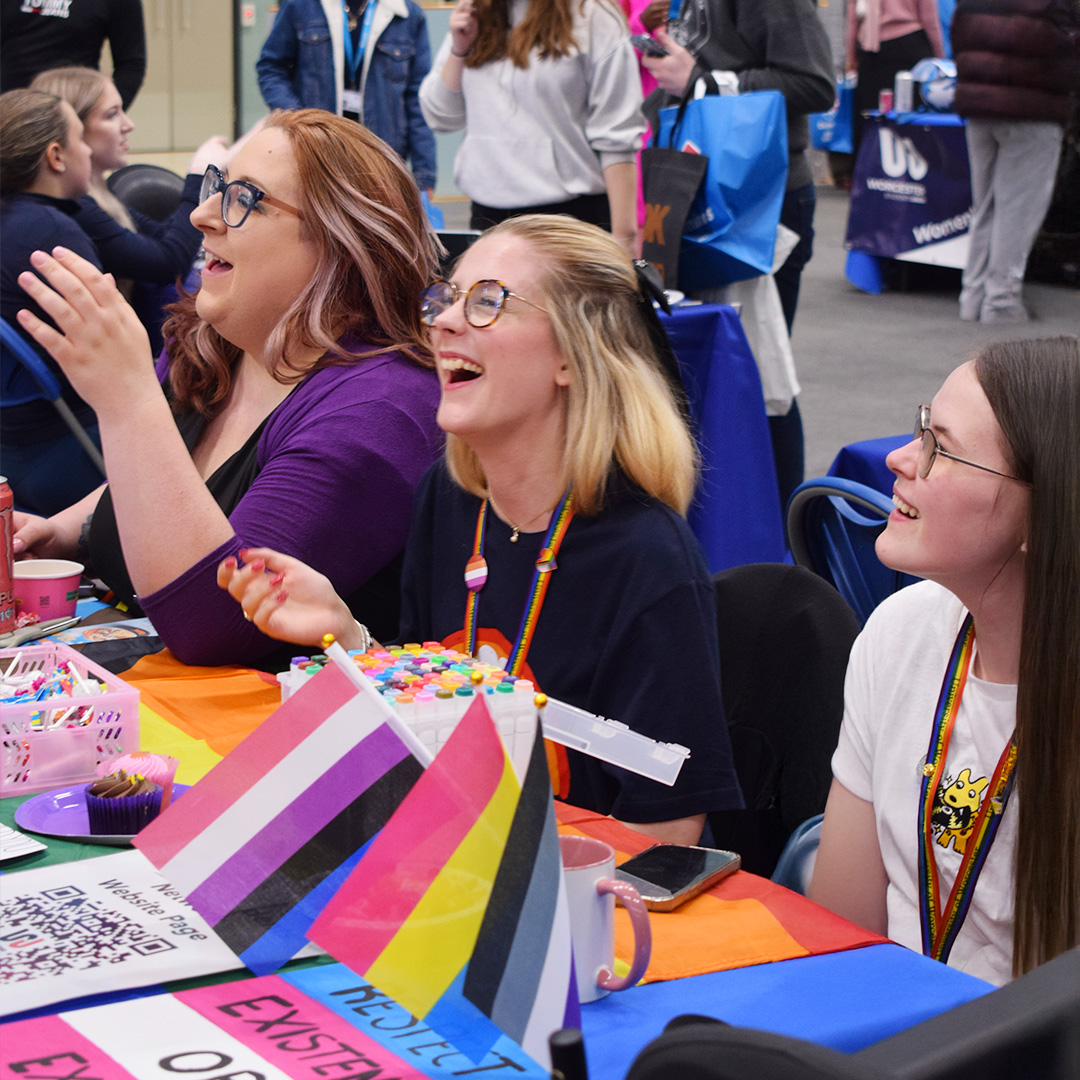 A stall at the Welcome Fair, with three students laughing