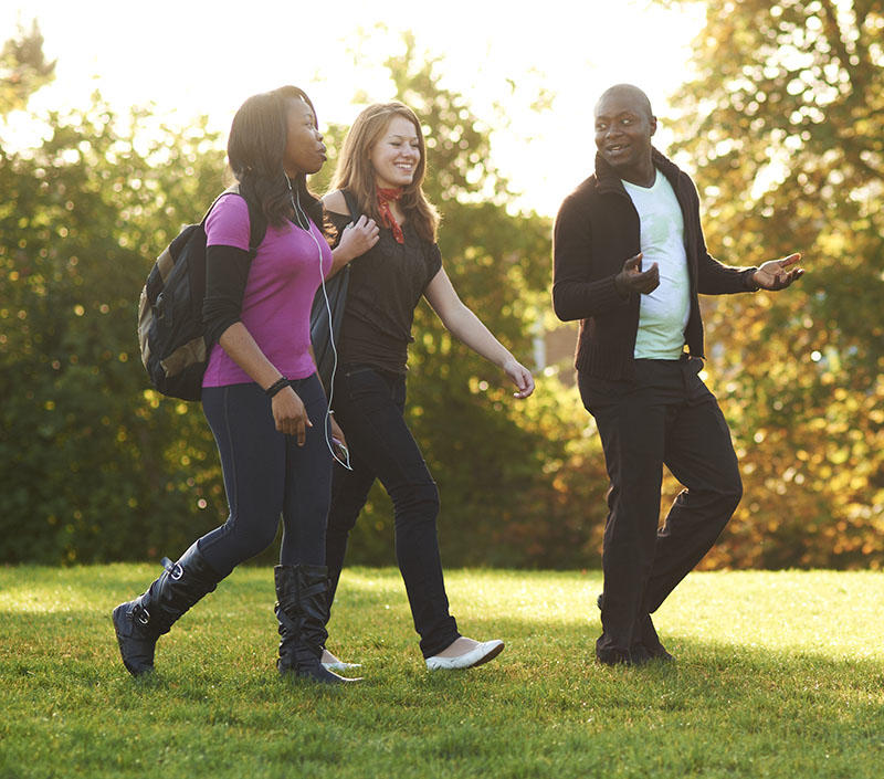 three students are walking in leafy surroundings