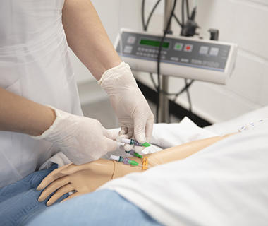 Shot of a dummy being given injected medication by a nurse wearing white rubber gloves.